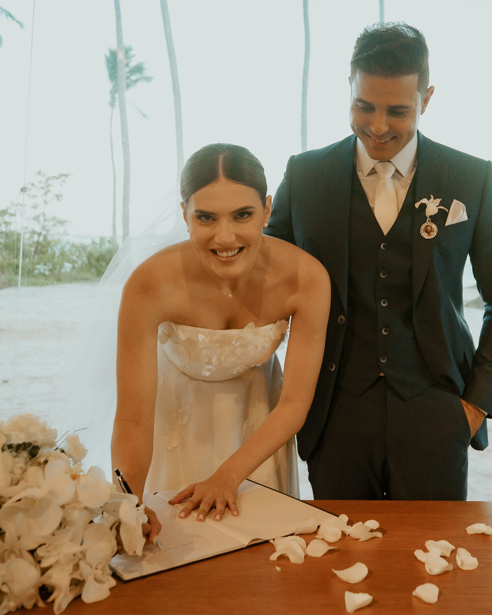 Thalita assina o livro de casamento à beira-mar, ao lado de Léo.